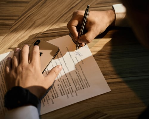 A person signing a lease agreement on a wooden desk with a smartphone placed nearby, symbolizing the process of securing a doctor office space for lease.